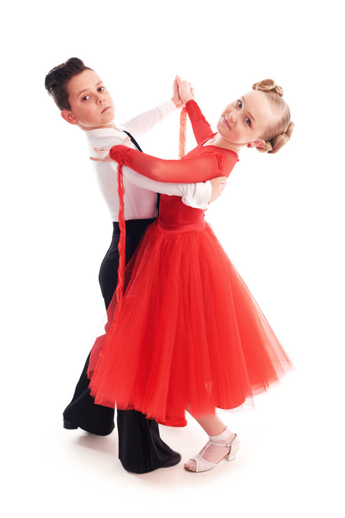 Young boy and girl smiling while practicing ballroom dance in a studio