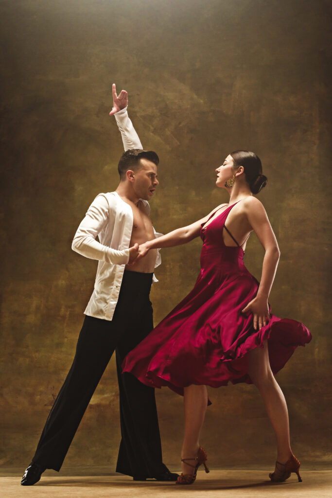 The young dance ballroom couple in red dress dancing in sensual pose on studio background. Professional dancers dancing tango. Ballroom dance concept. Human emotions - love and passion